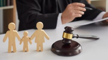 Close up of wooden figurines of family with child and gavel on background of judge conducting divorce process. Concept of alimony, family law and child custody.