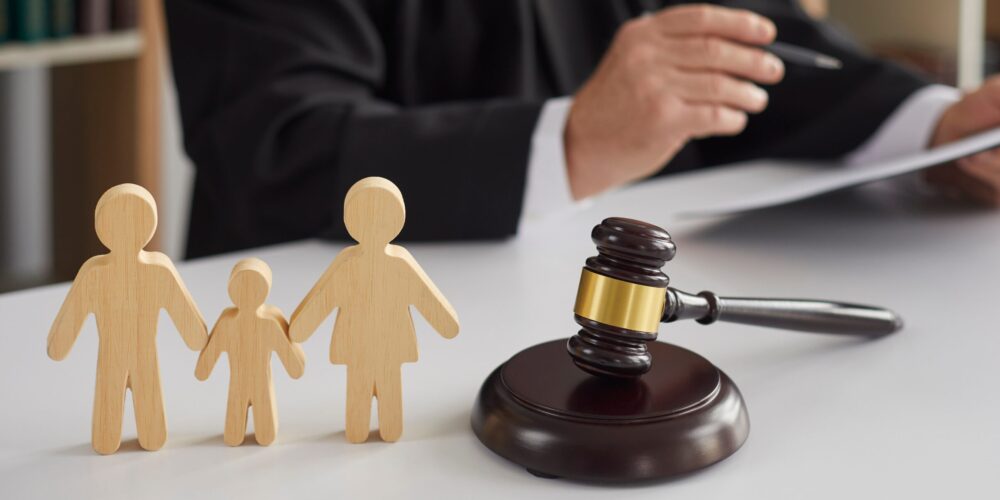 Close up of wooden figurines of family with child and gavel on background of judge conducting divorce process. Concept of alimony, family law and child custody.